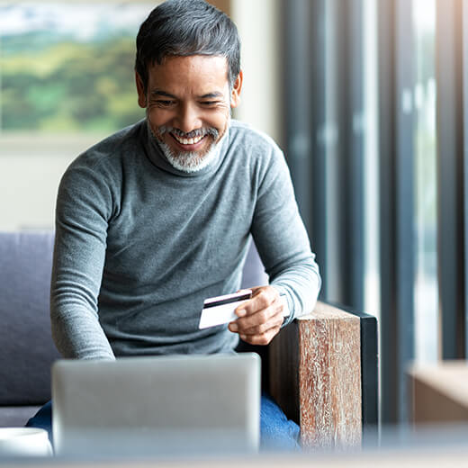 a middle aged man holding his credit card, smiling and doing something on his computer