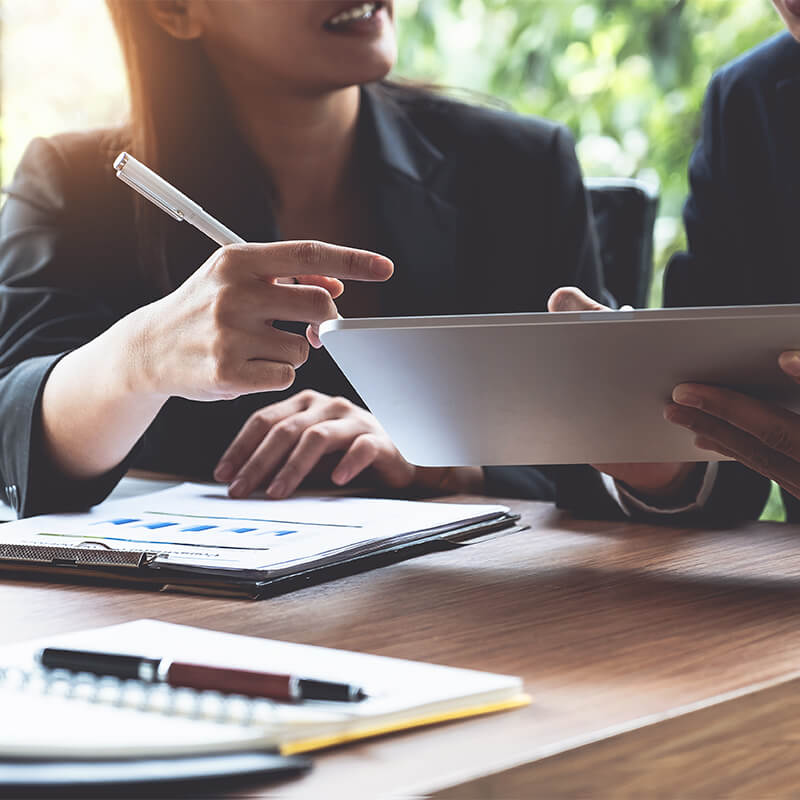 Financial consultation in progress, with advisor pointing at digital tablet displaying investment portfolios, emphasizing personalized wealth management.