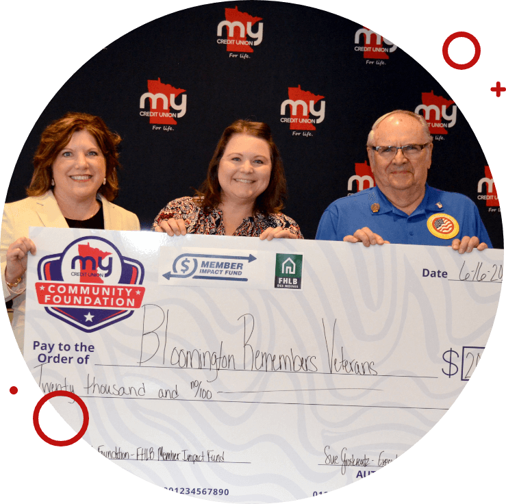 Three My Credit Union Community Foundation representatives smiling and holding a $20,000 ceremonial check made out to Bloomington Remembers Veterans against a branded backdrop.